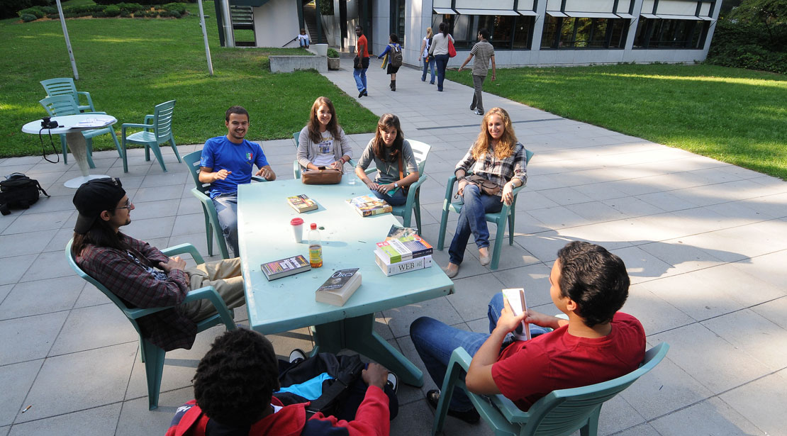 A group of students studies at a table in an open-air courtyard at our campus in Geneva.