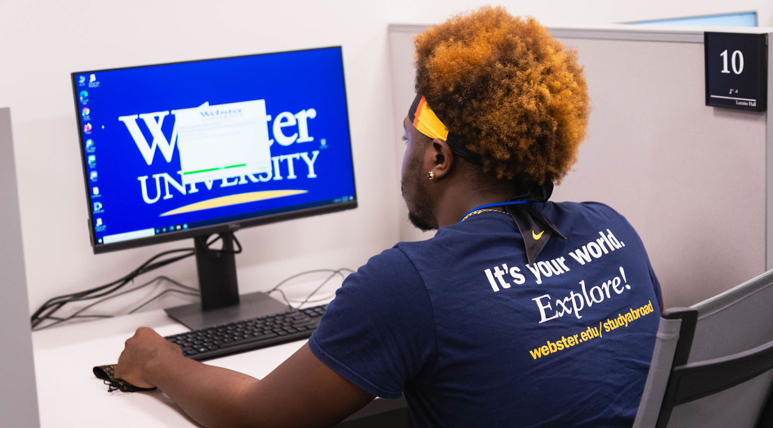 In the Reeg Academic Resource Center's testing site, a young dark-skinned male student with orange curly hair sits in front of a computer monitor.