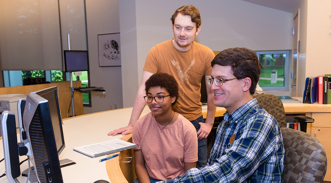 Three students looking at a project on laptop, smiling.