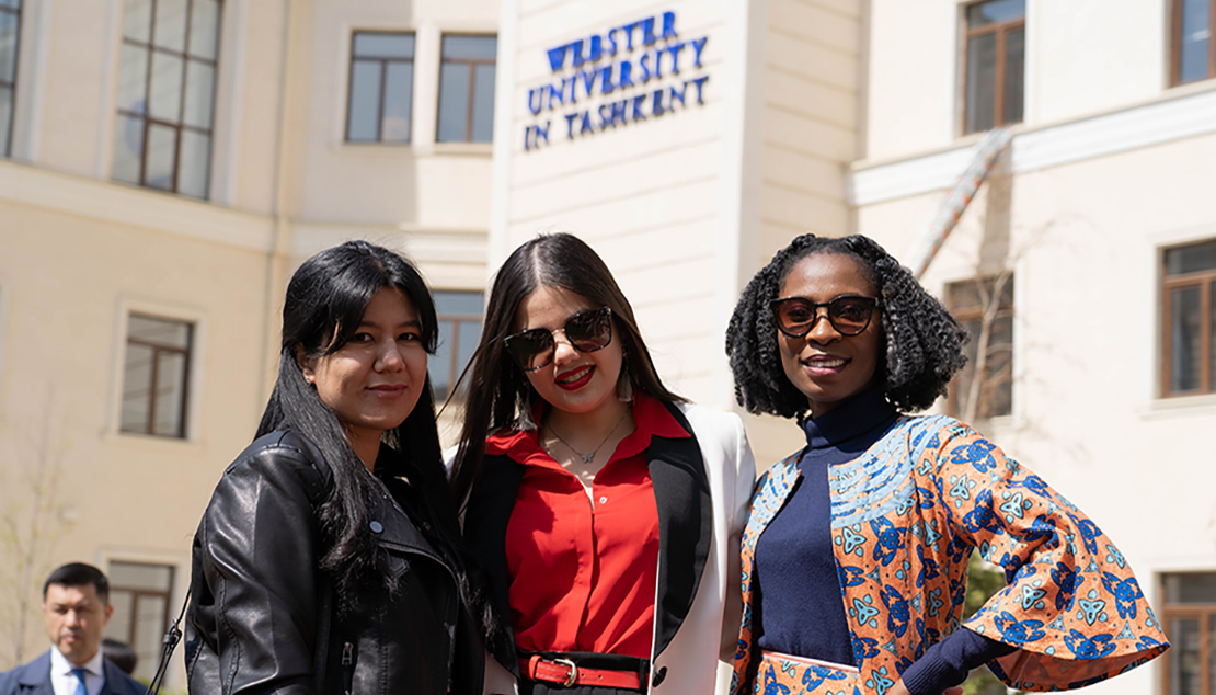 Three women stand together in front of Ӱҵ Tashkent sign with a man standing to the side of them..