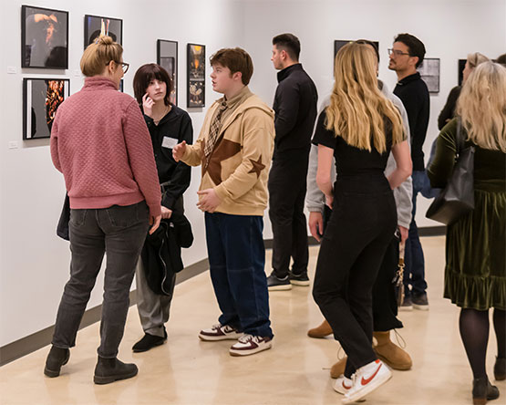 Gallery walls with photos and large group of people looking and talking