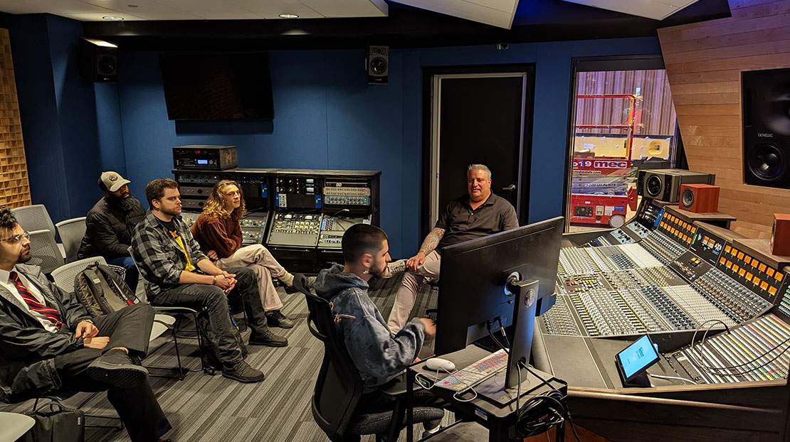 A professor teaches students in a recording/mixing room.