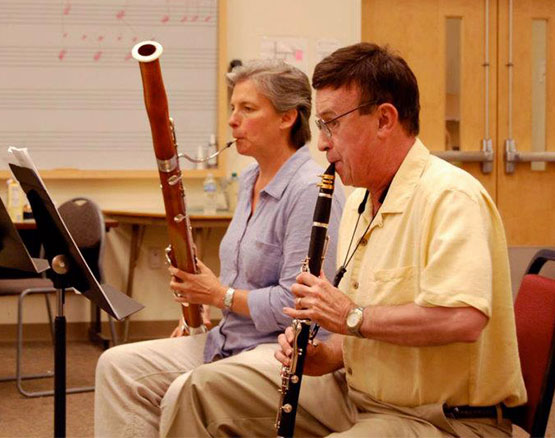 older woman playing bassoon and middle-aged man playing clarinet