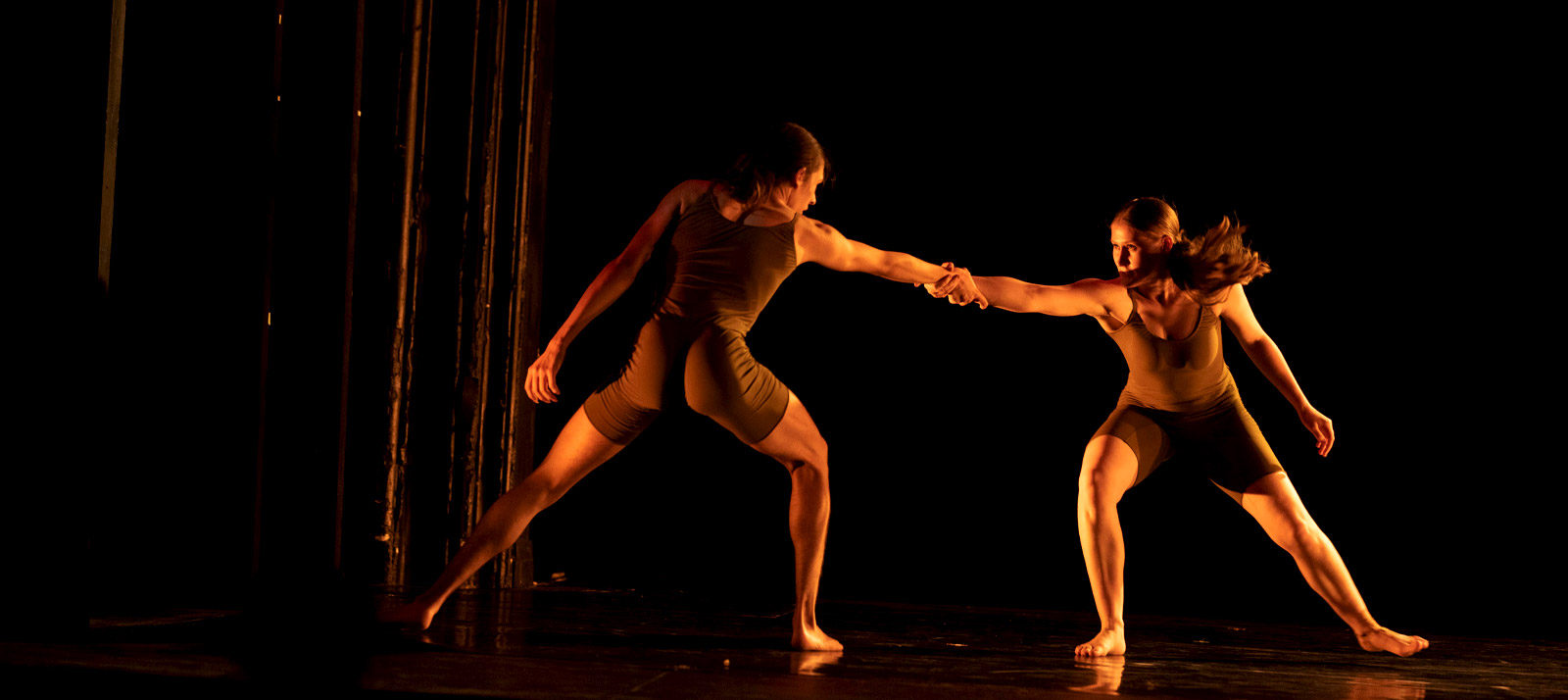 Two dancers reach their hands out for each other.