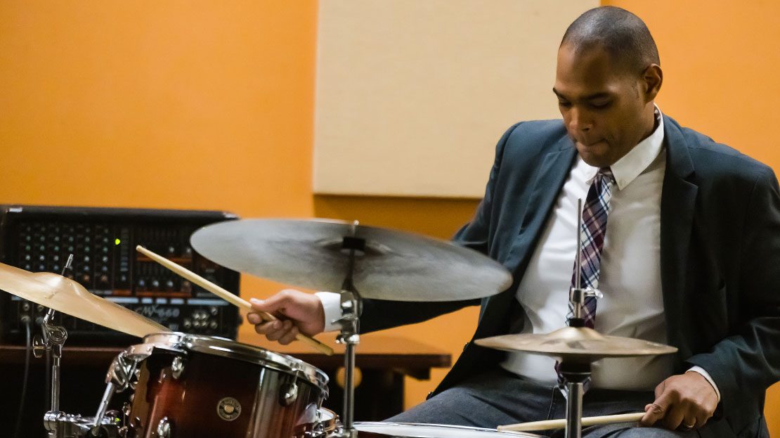 A drummer in a suit plays a set of drums.