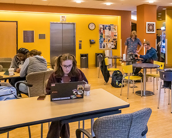 Students sitting at library cafe tables with laptops studying