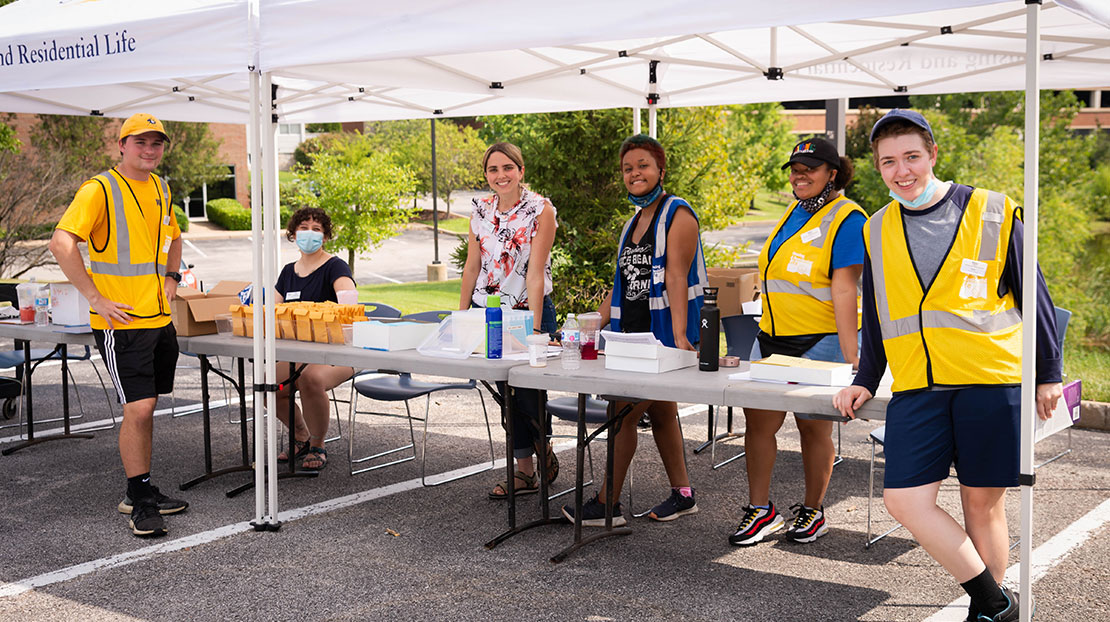 Housing staff stand at welcome table under event tent during move-in