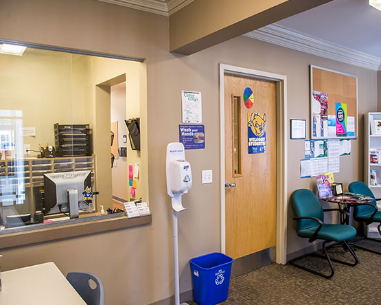 Student clinic waiting room with chairs, reception window, hand sanitizer dispenser