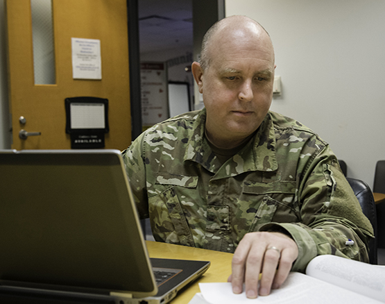 Male student in military fatigues working on a laptop for an online class. 