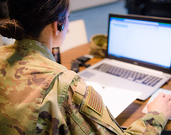 Female student in military fatigues working at a laptop on an online class. 