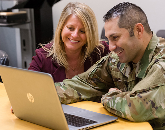 Military student and professor sit together at table looking at laptop 