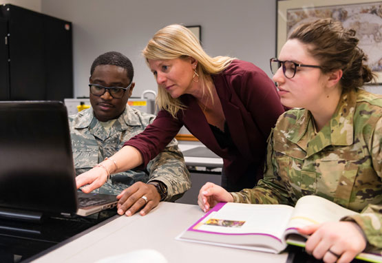 military students work with professor who points at computer screen