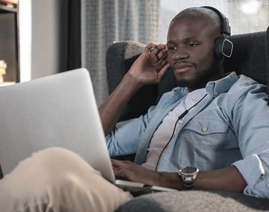 Man sits on couch with laptop while wearing headphones.
