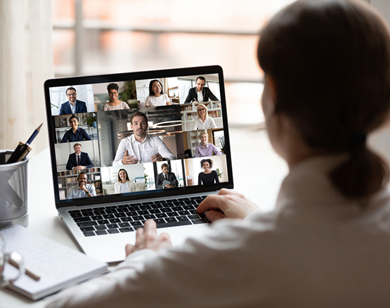 Woman sits in front of laptop with multiple people teleconferencing on screen.