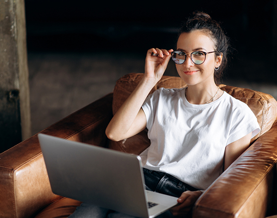 Woman sitting in comfy chair with laptop in lap adjusts her glasses