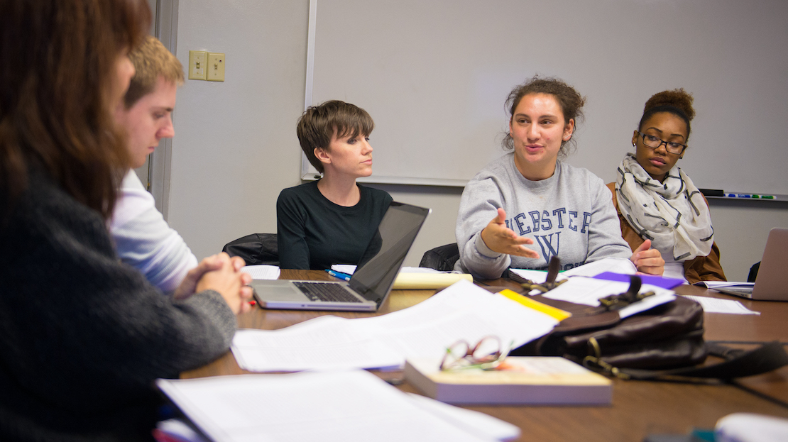 Students in class, discussing texts at a table.