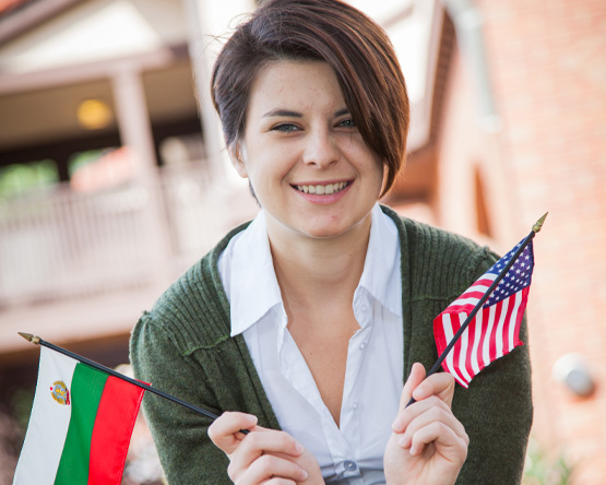 A student smiling and waving two miniature flags.