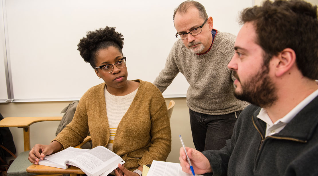 Two students and professor in class in a discussion. 