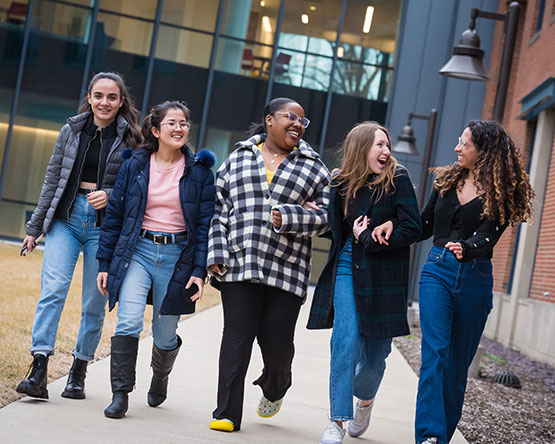 Five students walking with arms linked on Webster campus